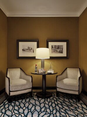 A hotel room with two armchairs, a table with a lamp, framed pictures on the wall, and a patterned carpet. - The One Monumental Palace (Porto)