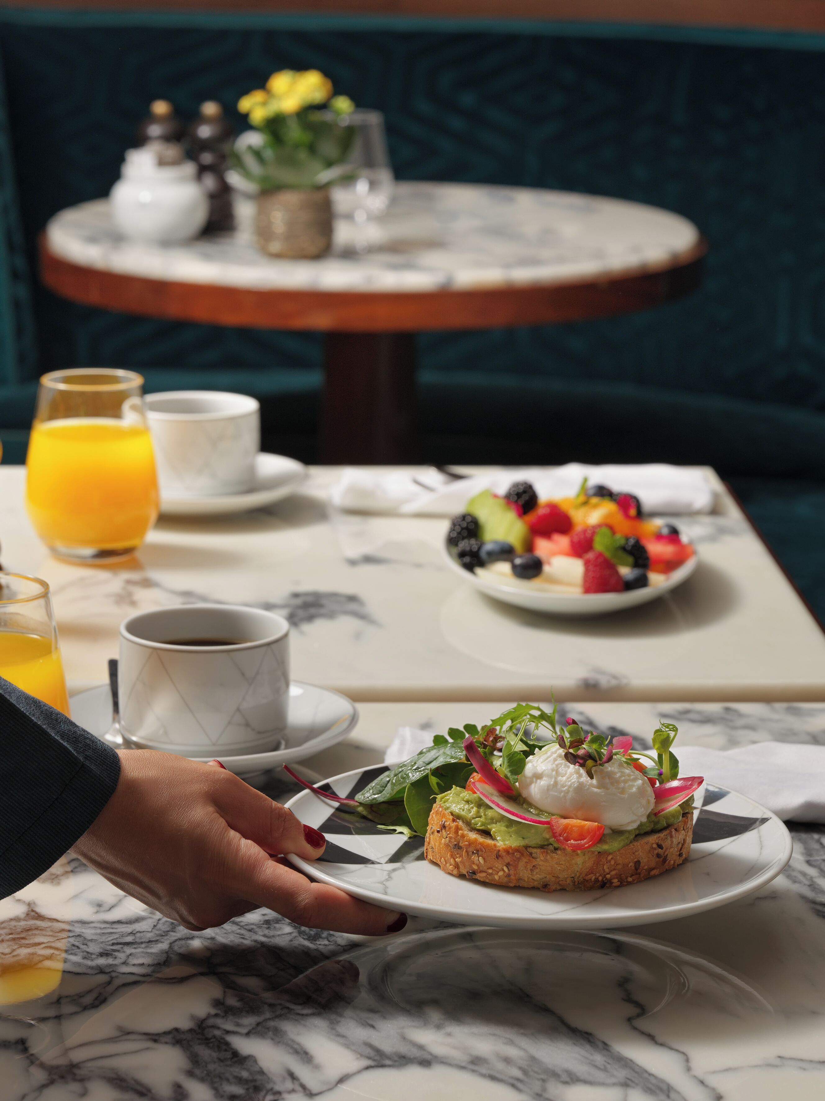 Uma mesa de mármore com um prato de comida, uma xícara de café e um copo de suco de laranja.