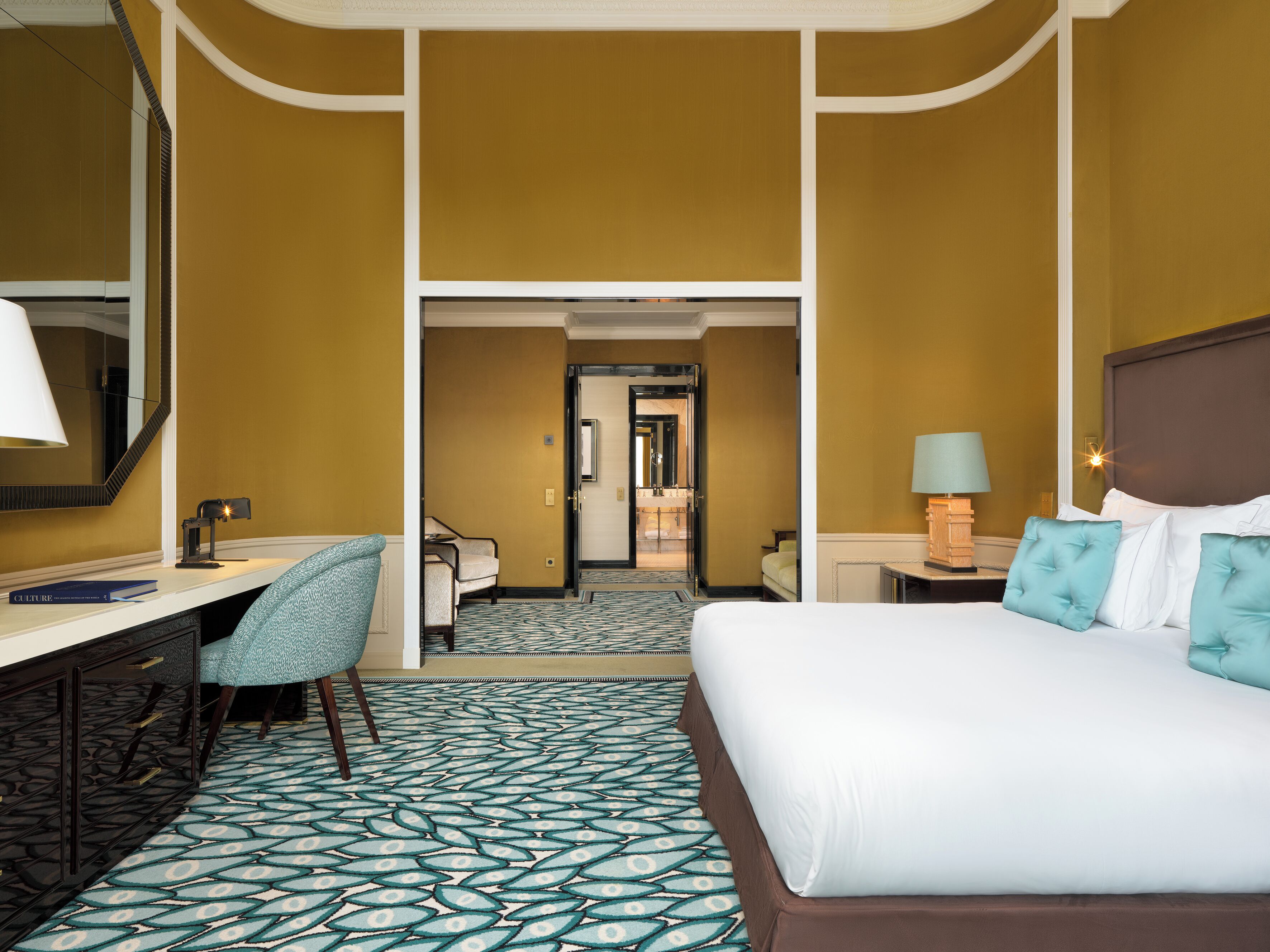 Habitación de hotel con cama, escritorio, silla y baño visible a través de una puerta abierta.