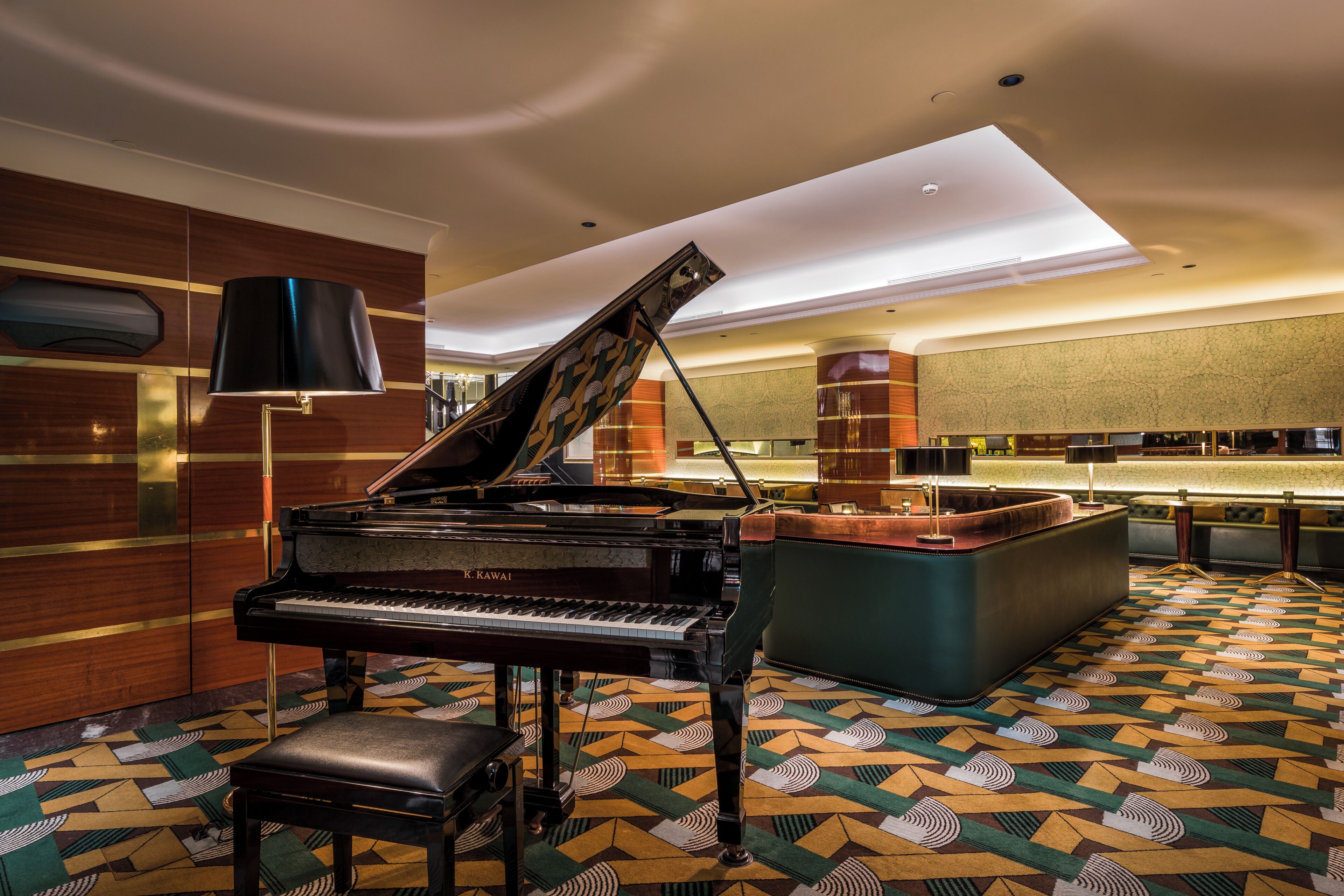 A grand piano in a spacious room with patterned carpet, a bar area, and a modern ceiling design.