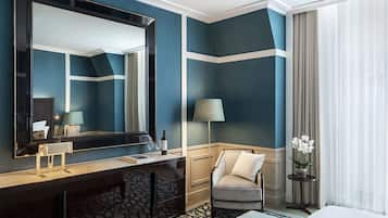 Habitación de hotel con un espejo grande, una tocador con lámpara, una silla, una mesita de noche con un florero y una cama.