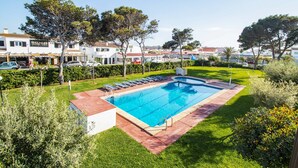 A rectangular swimming pool with a red border, surrounded by a well-maintained lawn and trees. - Apartamentos Sol Y Mar Menorca (Ciutadella de Menorca)