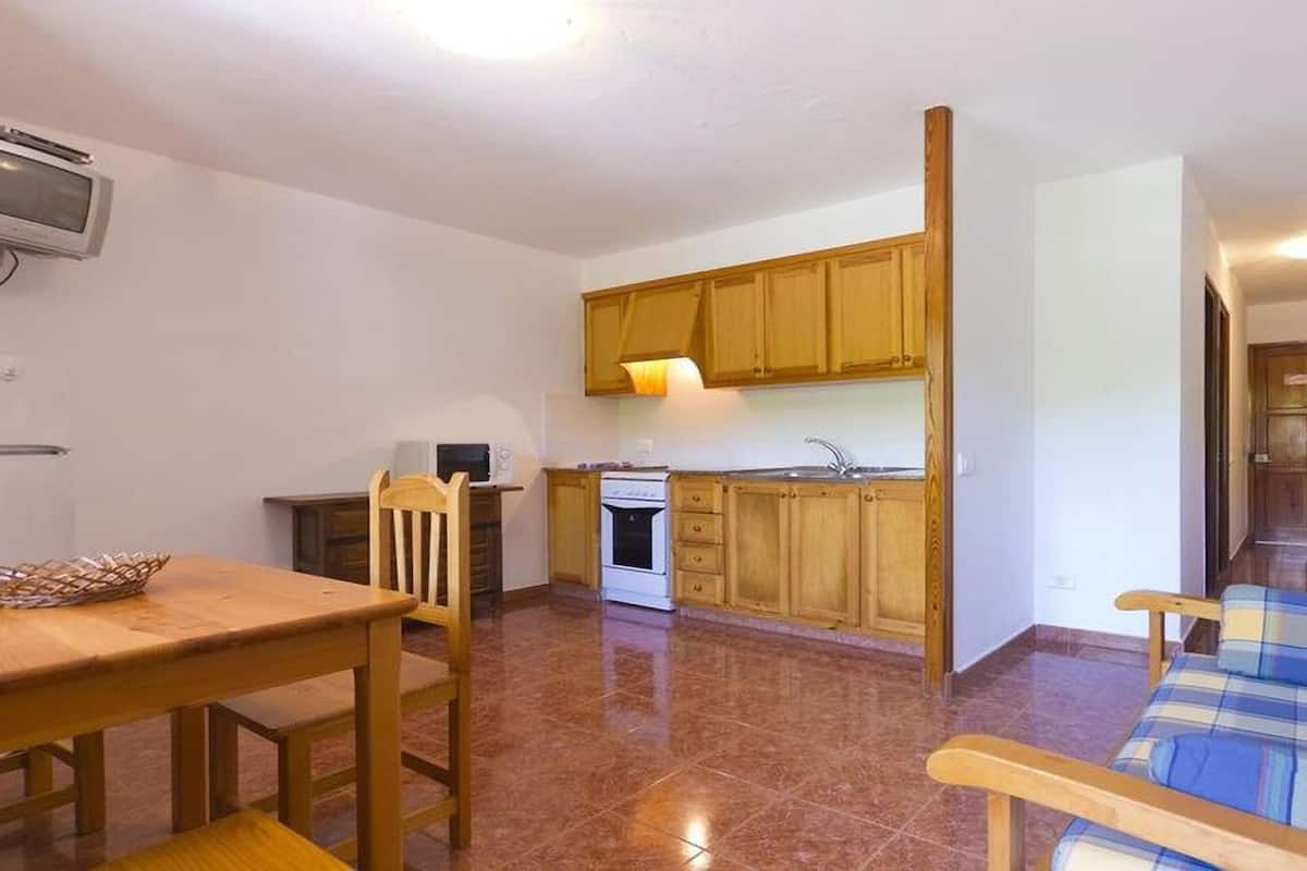 Eine kompakte Küche mit Holzausstattung, einer Mikrowelle und einem Herd. Im Wohnbereich befindet sich ein Esstisch mit Stühlen sowie eine Couch.