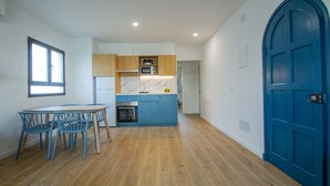 A modern kitchen with wooden cabinets, a blue countertop, and a built-in oven. There is a dining area with a table and chairs. - Apartamentos Sol Y Mar Menorca (Ciutadella de Menorca)