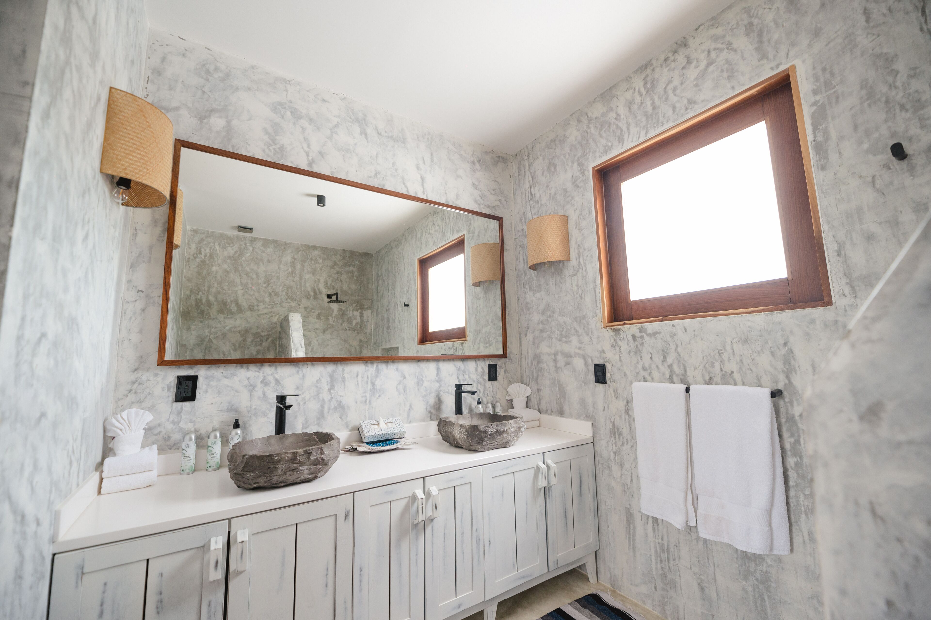 A bathroom with marble walls, a large mirror, a wooden-framed window, and a white vanity with a stone basin.