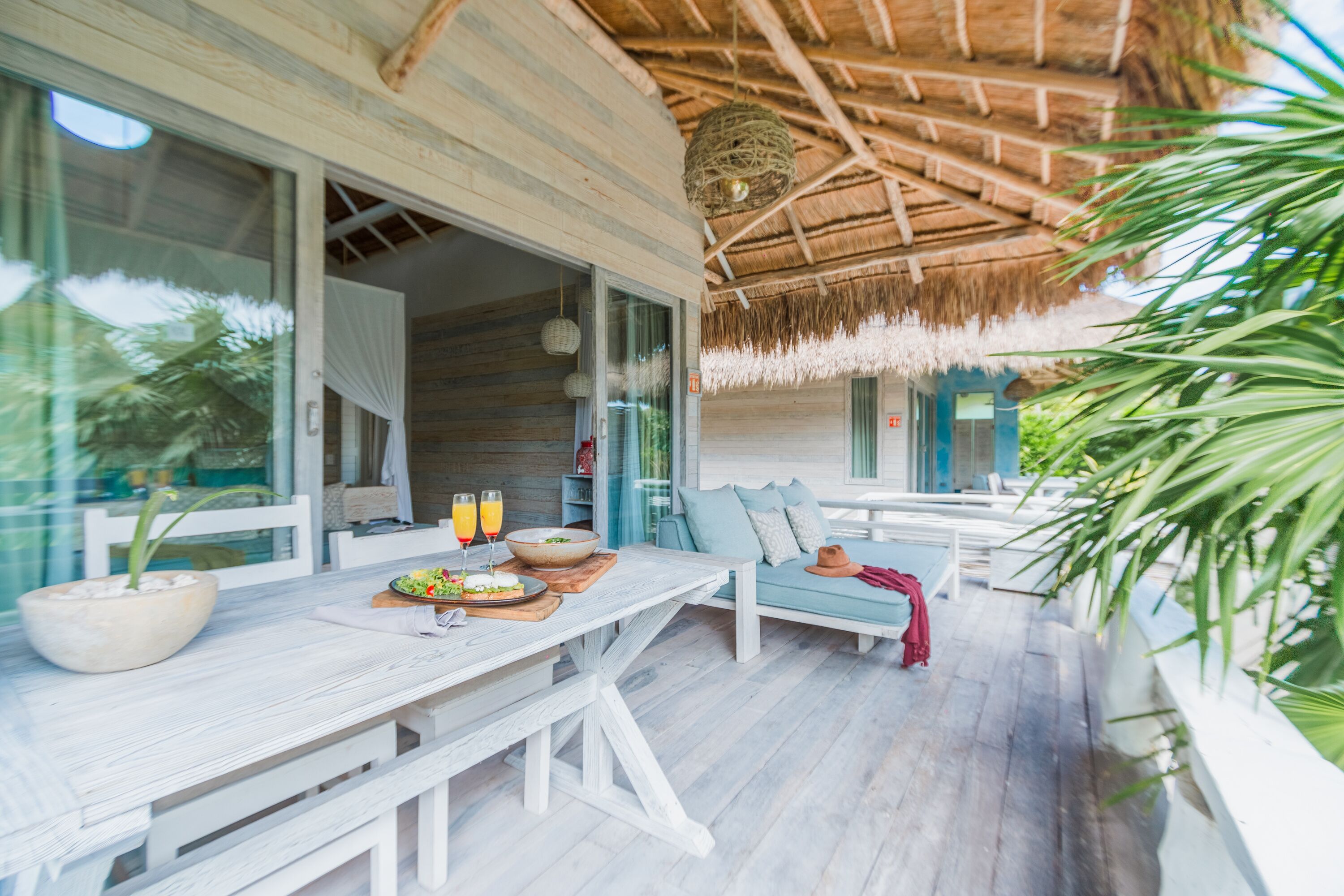 A covered outdoor seating area with a table set for two, a bench, and a hanging light fixture.