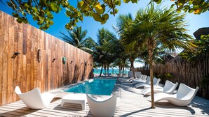 Une terrasse en bois avec une piscine, des chaises longues blanches, des palmiers et un mur en bois.