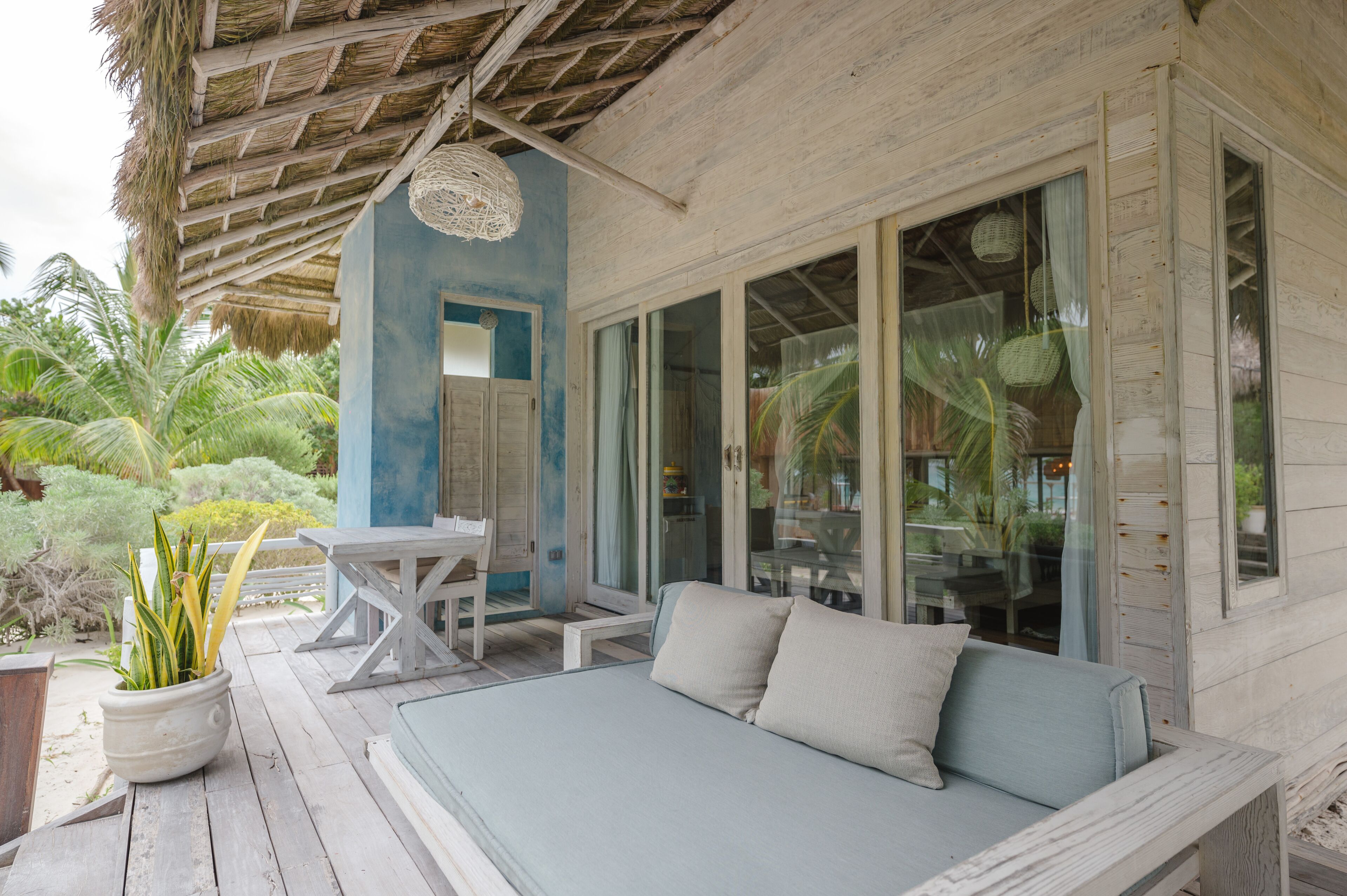 Una terraza de madera con un sofá azul claro y una mesa, rodeada de puertas y ventanas de vidrio.