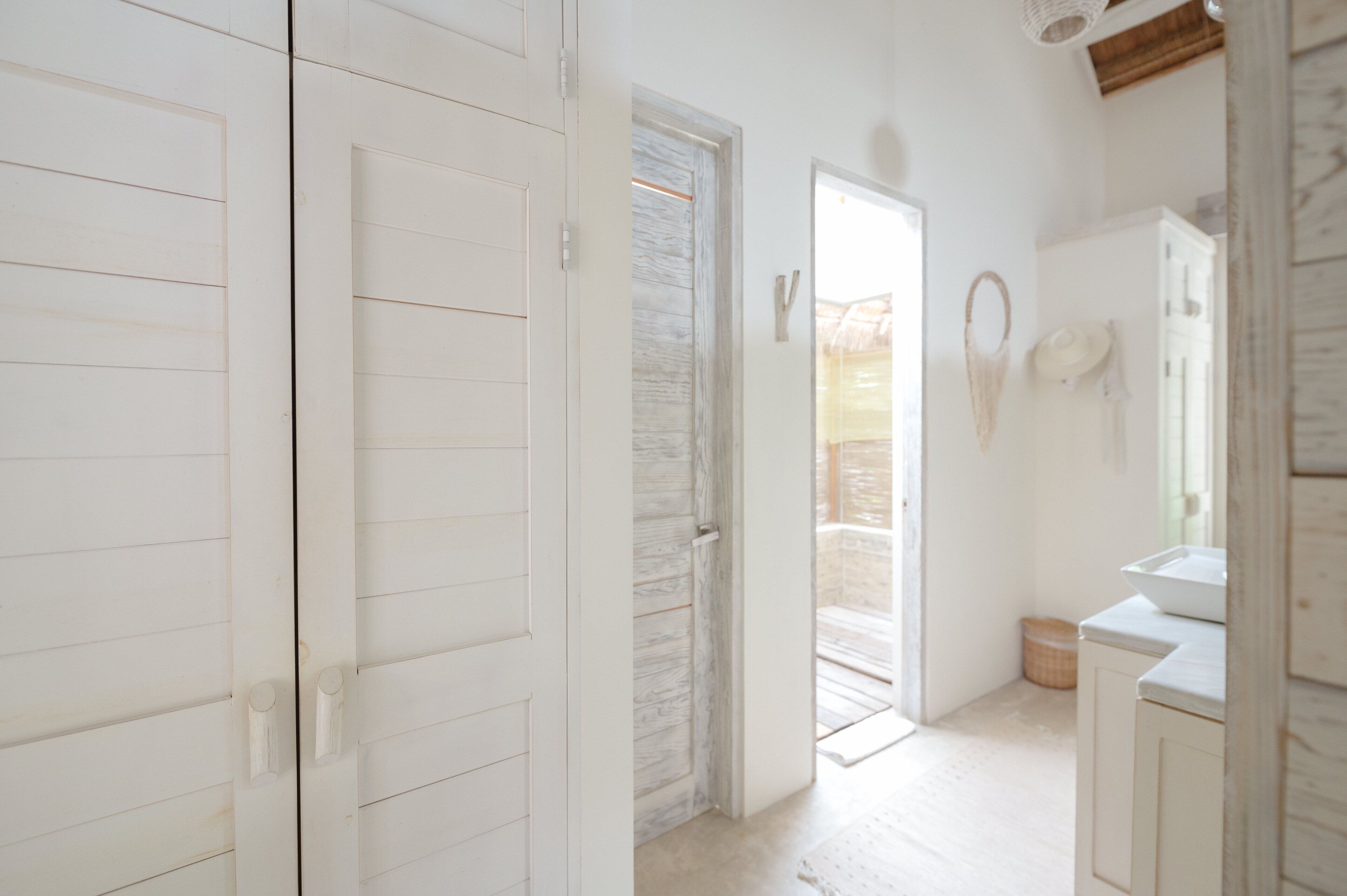 A hallway with white wooden doors, a white marble wall, and a white sink.