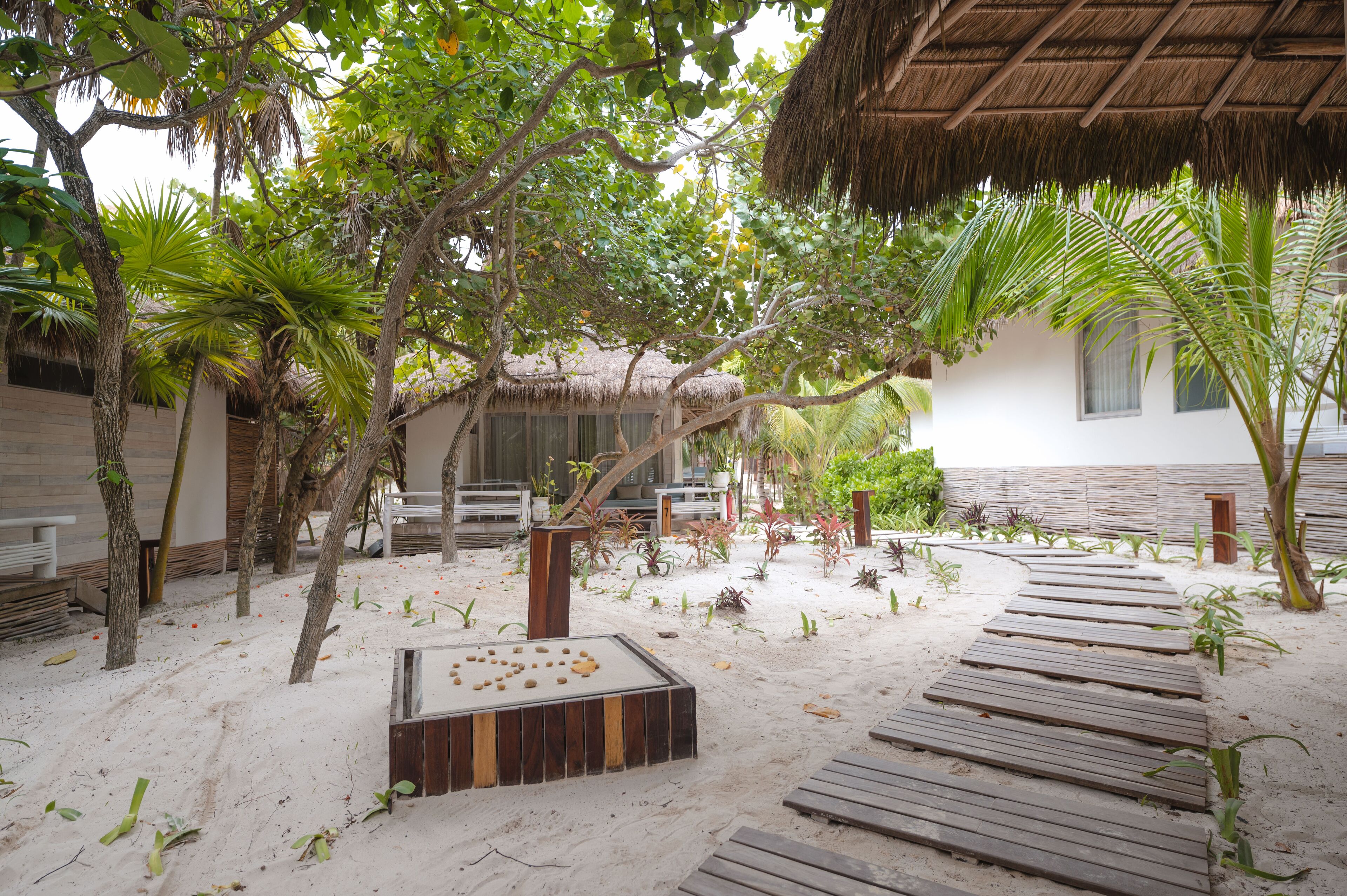 A tropical resort with a thatched-roof hut, wooden deck, and lush greenery.