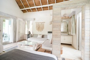 Un dormitorio moderno con una cama grande, una mesa de centro de vidrio, un sofá y un baño visible a través de una puerta abierta.