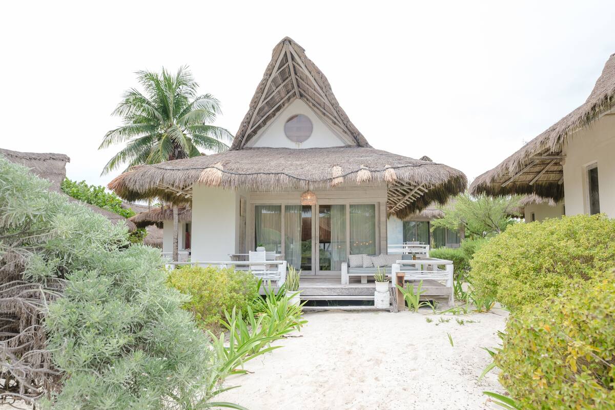 A beachfront property with thatched-roof huts, a sandy pathway, and lush greenery.