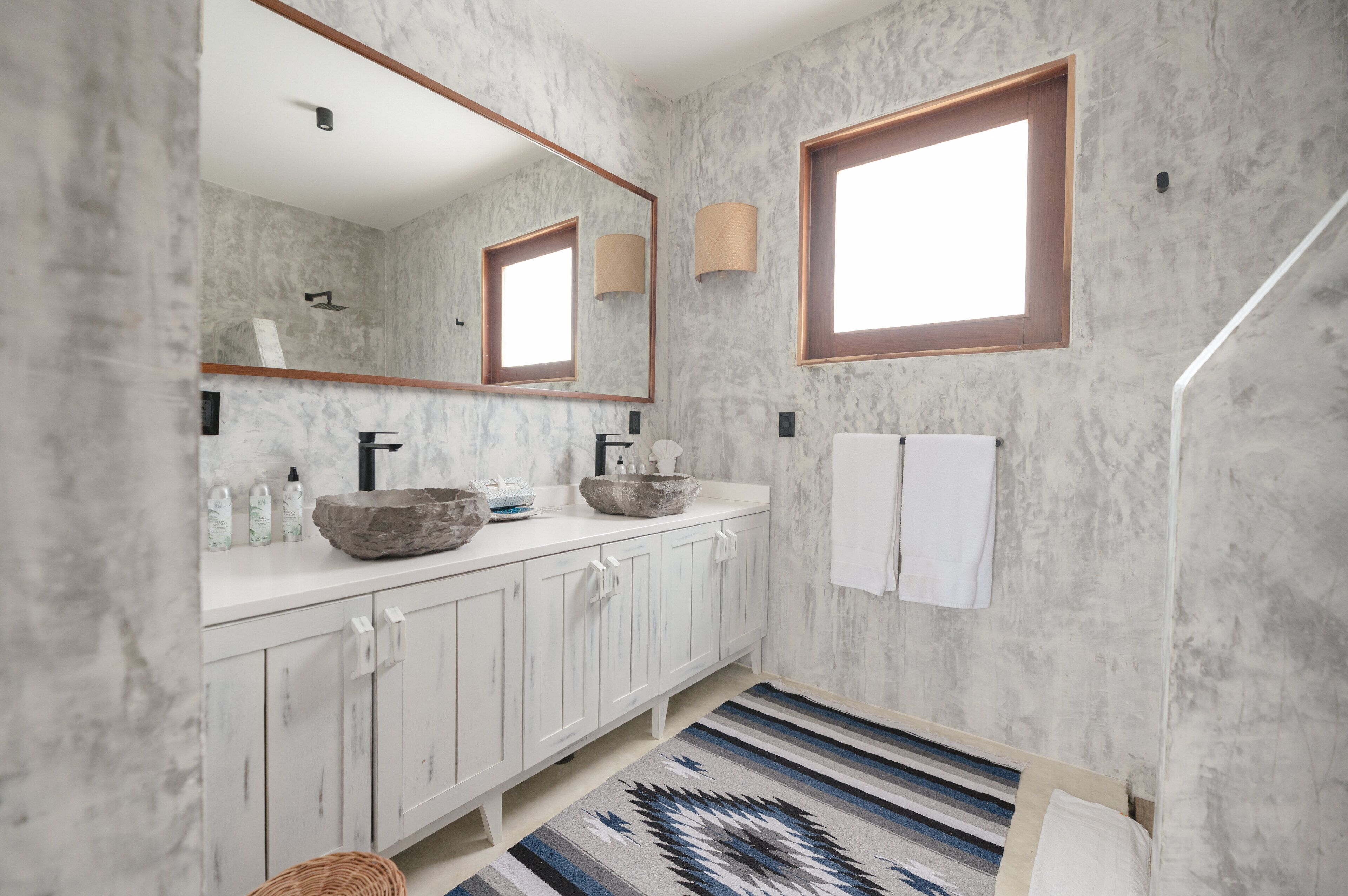A bathroom with marble walls, a large mirror, two sinks, a towel rack, and a patterned rug.