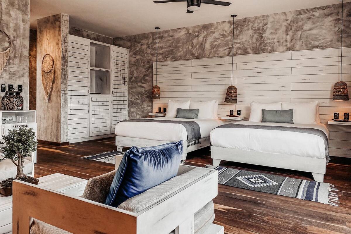 A modern bedroom with two beds, a wooden wardrobe, a ceiling fan, and a small side table with a lamp.