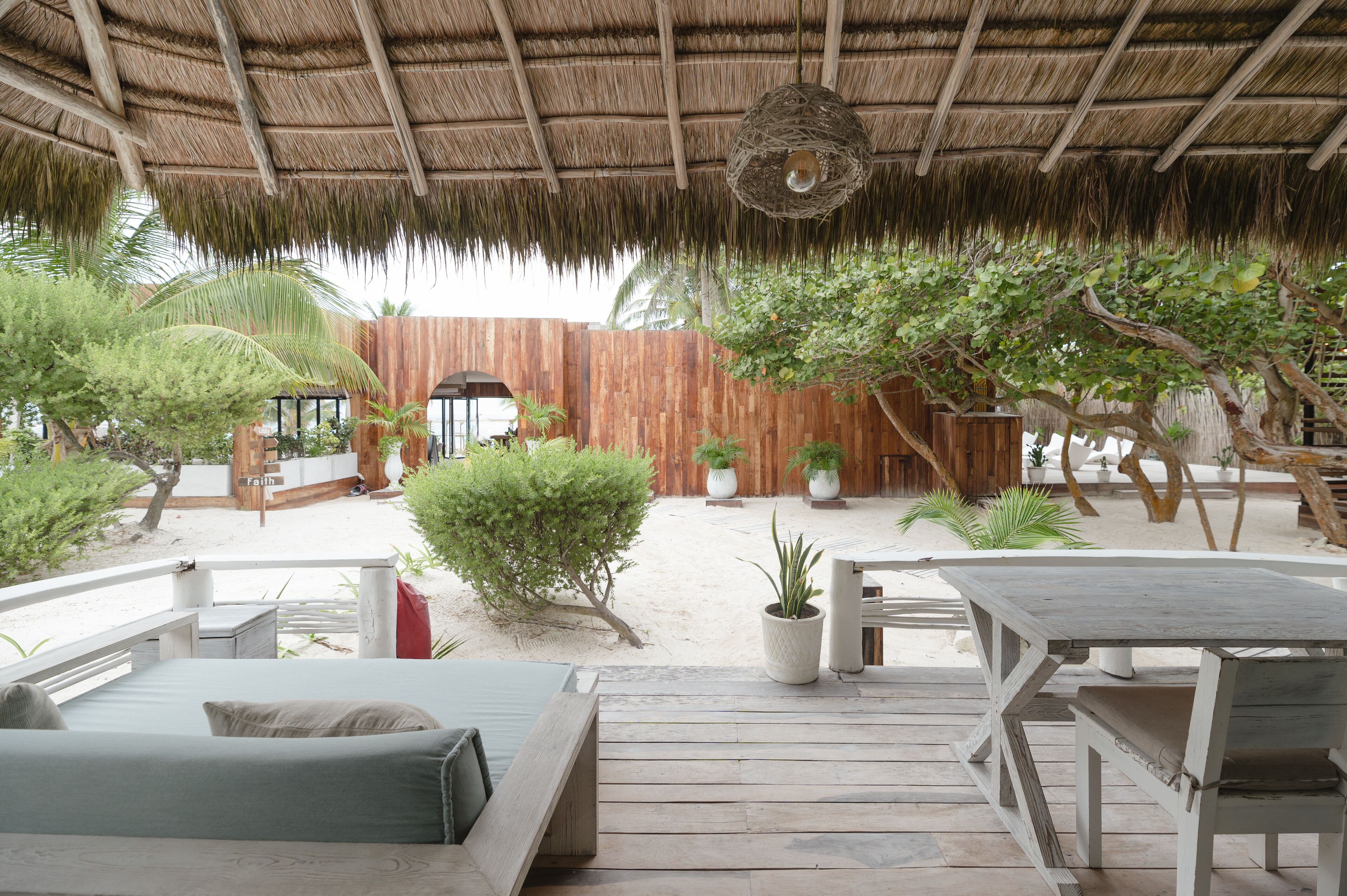 A wooden deck with a thatched roof, surrounded by potted plants and a wooden fence.