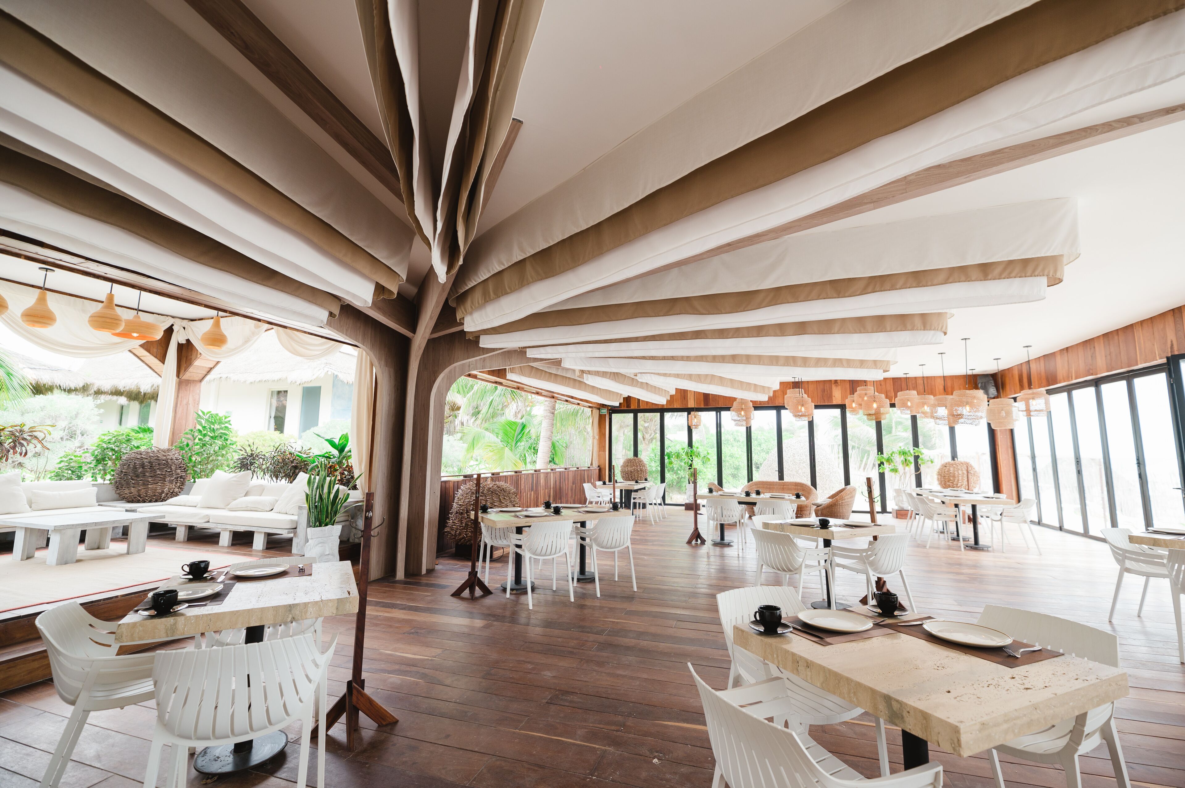 Un amplio comedor interior con suelo de madera, muebles blancos y grandes ventanales que dejan entrar luz natural.