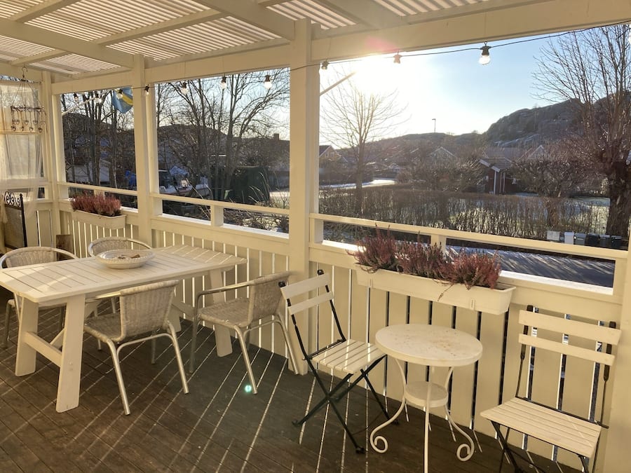 A covered patio with a table and chairs, a small round table, and a view of a lake and mountains.