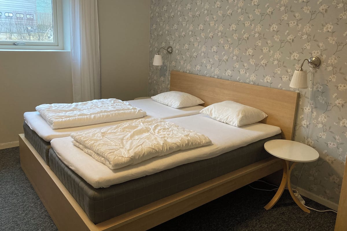 Una cama doble con dos almohadas, una mesita de noche y una lámpara de pared.