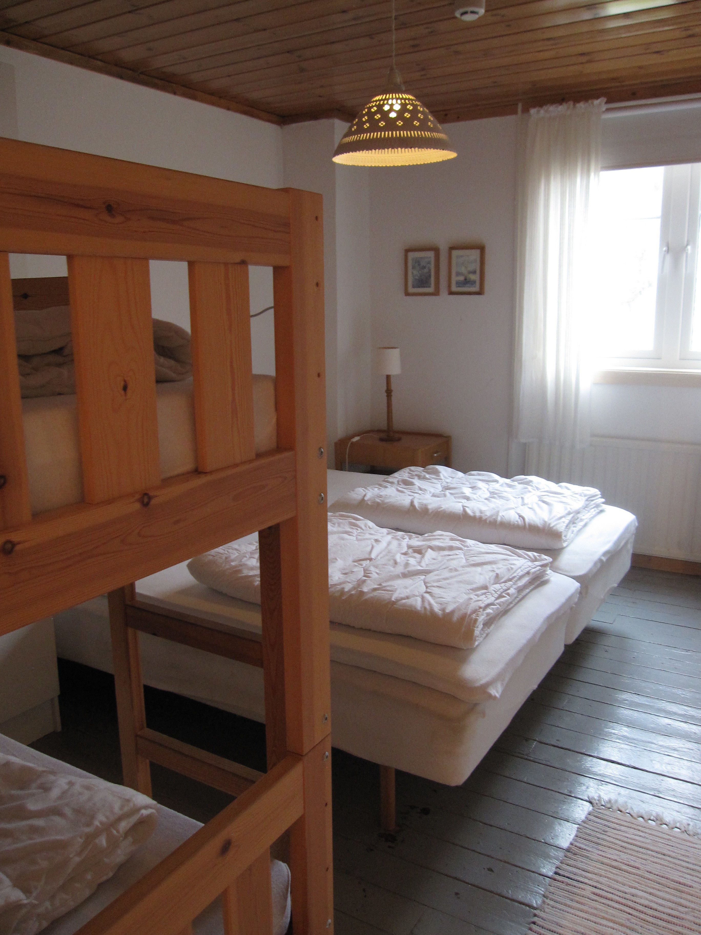Une chambre de dortoir avec des lits superposés, un plafond en bois, une lampe suspendue et une fenêtre avec des rideaux.