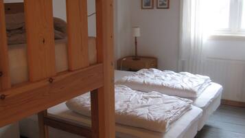 Une chambre de dortoir avec des lits superposés, un plafond en bois, une lampe suspendue et une fenêtre avec des rideaux.
