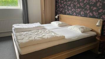 Una cama bien hecha con cabecera de madera, una mesita de noche con lámpara y una ventana con cortinas.