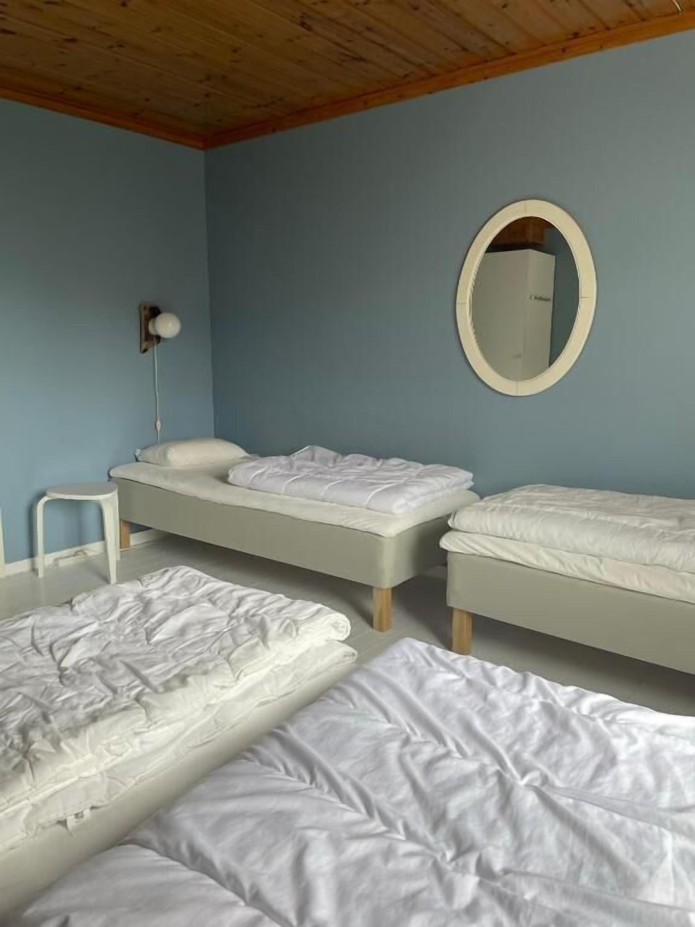 Una habitación con dos camas, un taburete pequeño y un espejo redondo en la pared.
