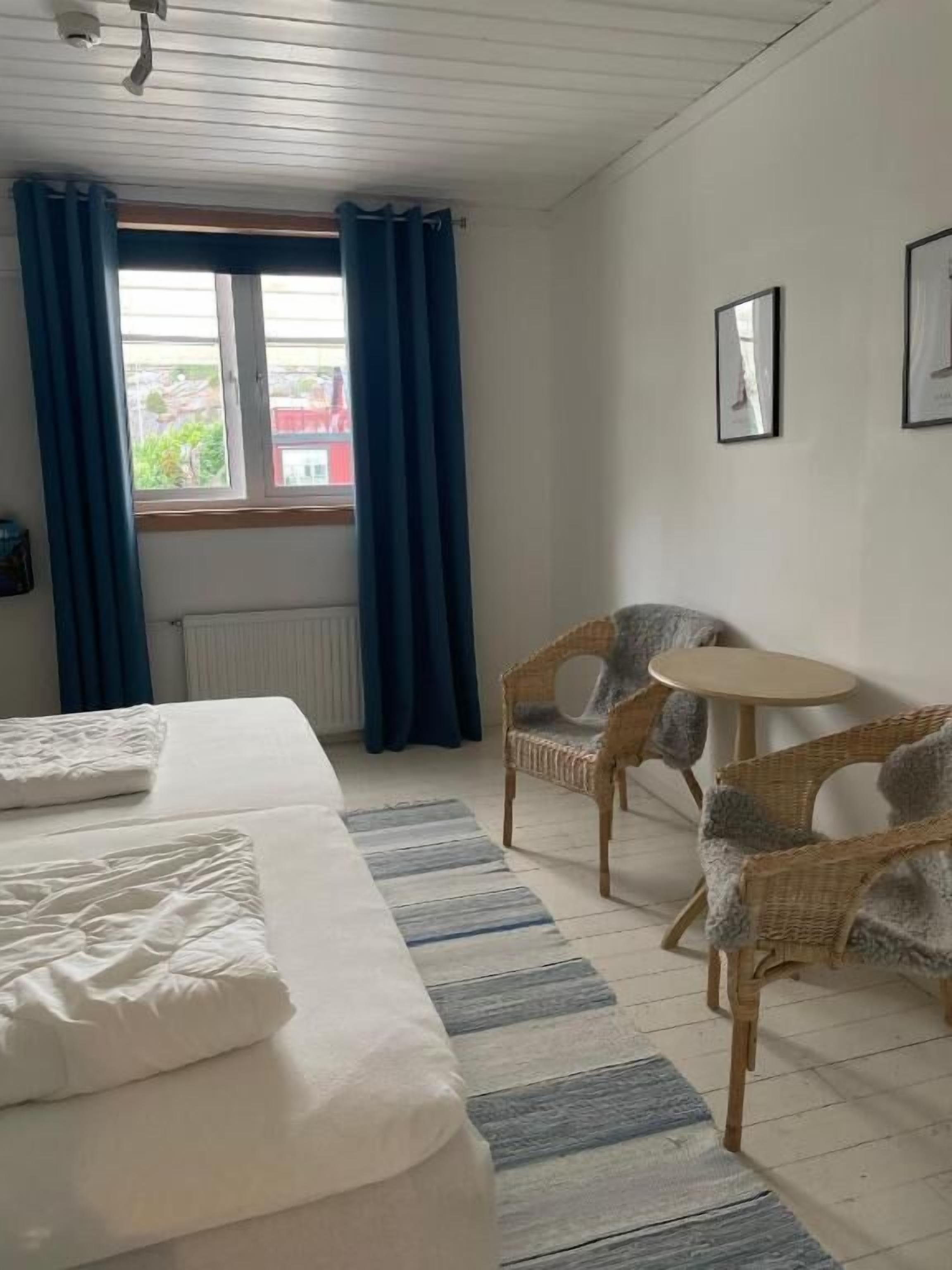 A bedroom with a bed, two wicker chairs, a small round table, and a window with curtains.