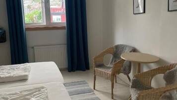 A bedroom with a bed, two wicker chairs, a small round table, and a window with curtains.