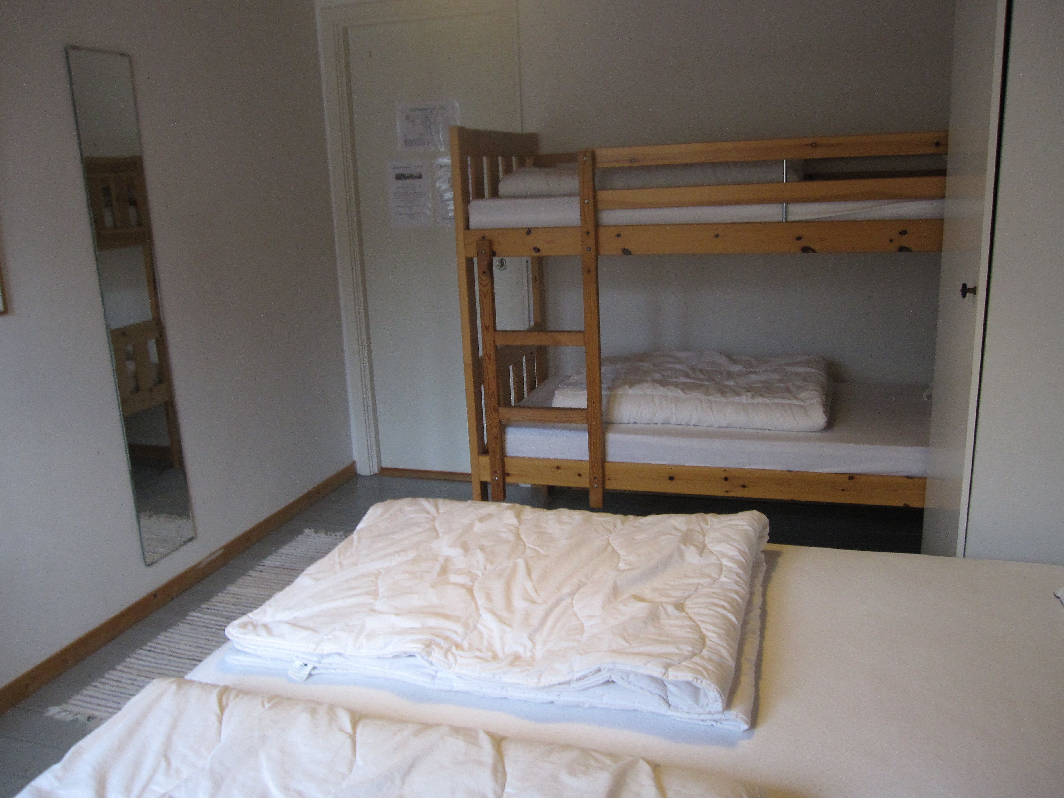 A bunk bed room with a wooden frame, a white mattress on the lower bunk, and a folded white blanket on the bed.