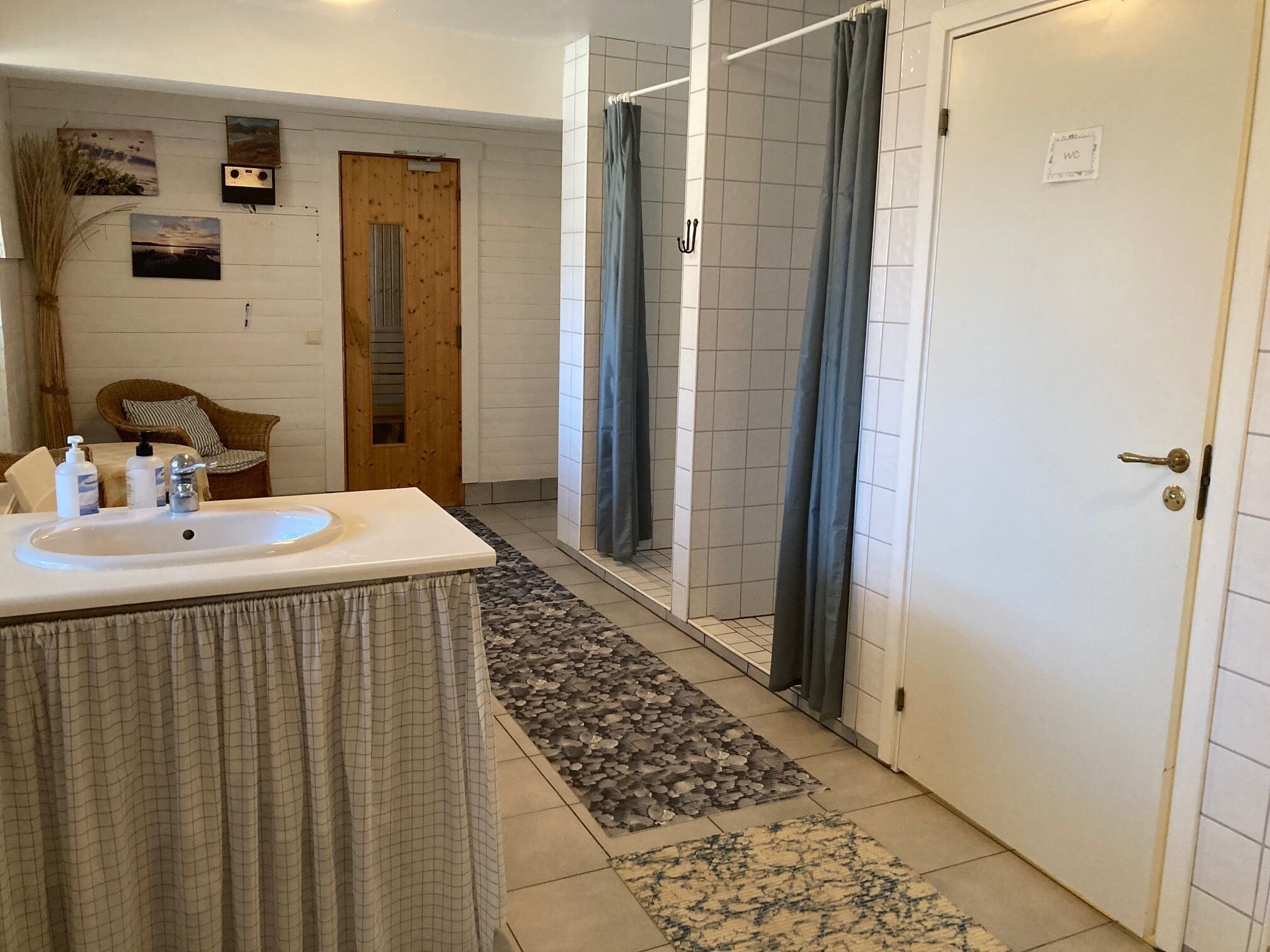 Uma casa de banho com lavatório, chuveiro e uma porta com a inscrição 'WC'.