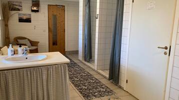 Uma casa de banho com lavatório, chuveiro e uma porta com a inscrição 'WC'.