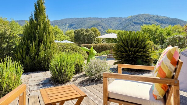 A wooden deck with a chair and umbrella, surrounded by lush greenery and a mountain view. - Casa Carvalhal - Adults Only (Góis)