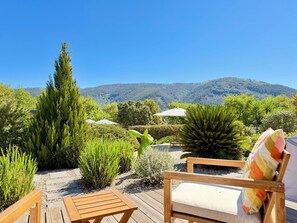 A wooden deck with a chair and umbrella, surrounded by lush greenery and a mountain view. - Casa Carvalhal - Adults Only (Góis)