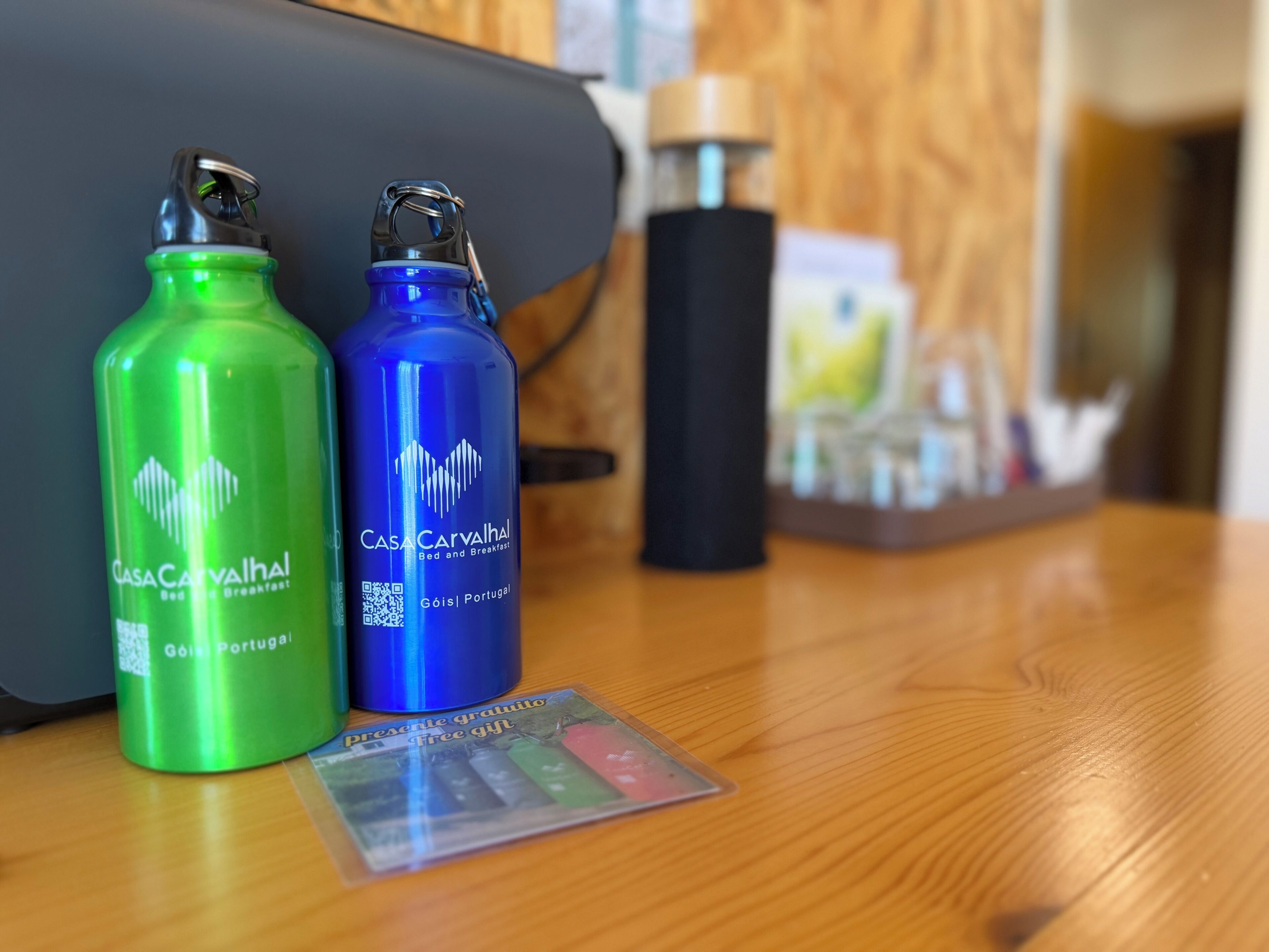 Two water bottles, one green and one blue, on a wooden table with a black object and a small card in the background.