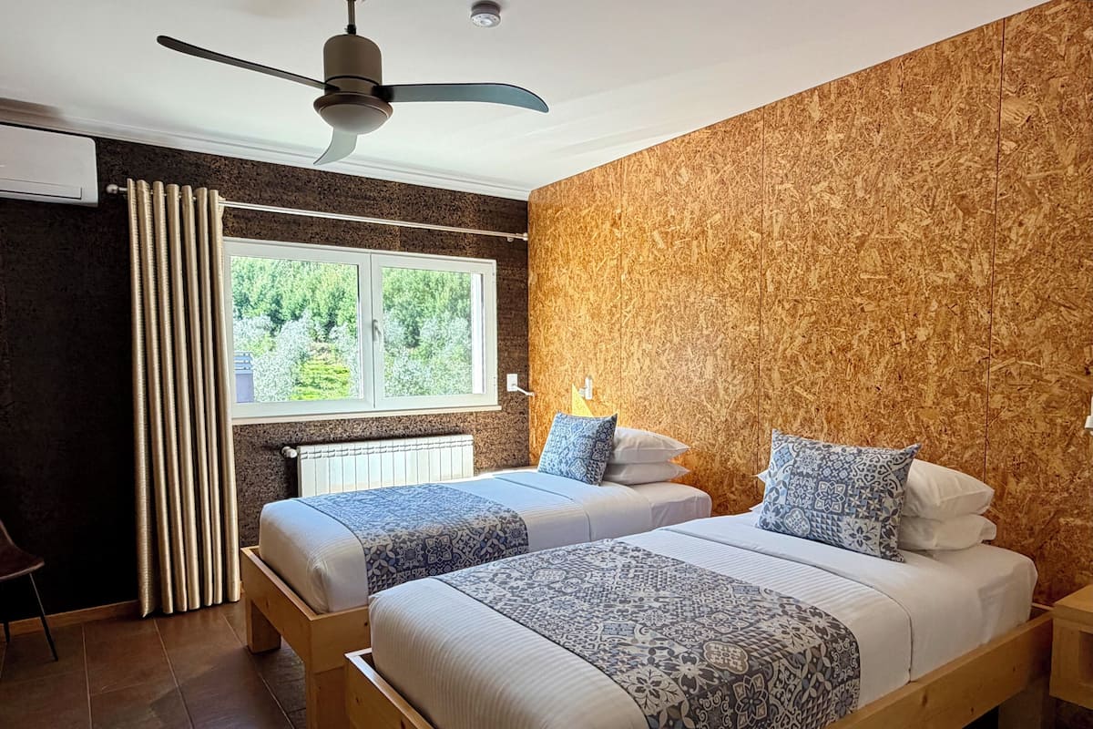 Un dormitorio con dos camas, una ventana con cortinas, un ventilador de techo y un radiador.