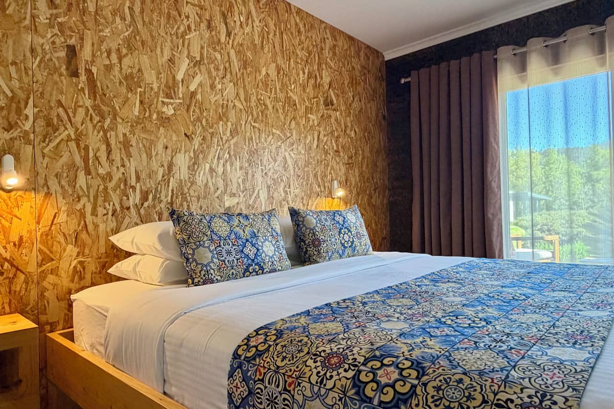 Un dormitorio con cama, ropa de cama estampada, una pared de madera y una ventana con cortinas.