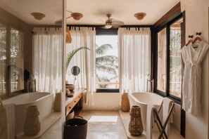A bathroom with a bathtub, a large mirror, a vanity with a sink, and a window with curtains.