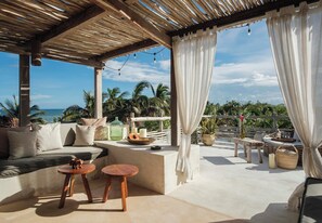 A covered outdoor seating area with a sofa, two small tables, and a view of the ocean.