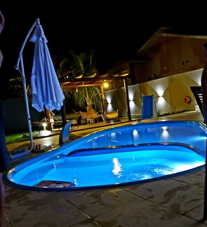 A swimming pool with a curved edge, surrounded by chairs and a covered umbrella. - Casa M&N (Foz do Iguaçu)