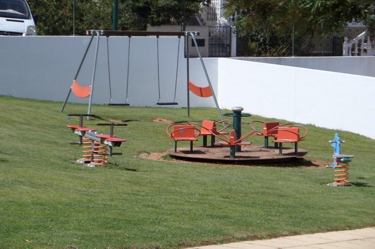 Ein Spielplatz mit Schaukeln, einer Karrusell und einer Wippe.