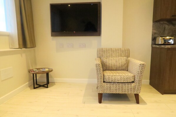 A living room with a patterned armchair, a small side table, a flat-screen TV mounted on the wall, and a wooden cabinet. - Quay Apartments Clarence House (Newport)