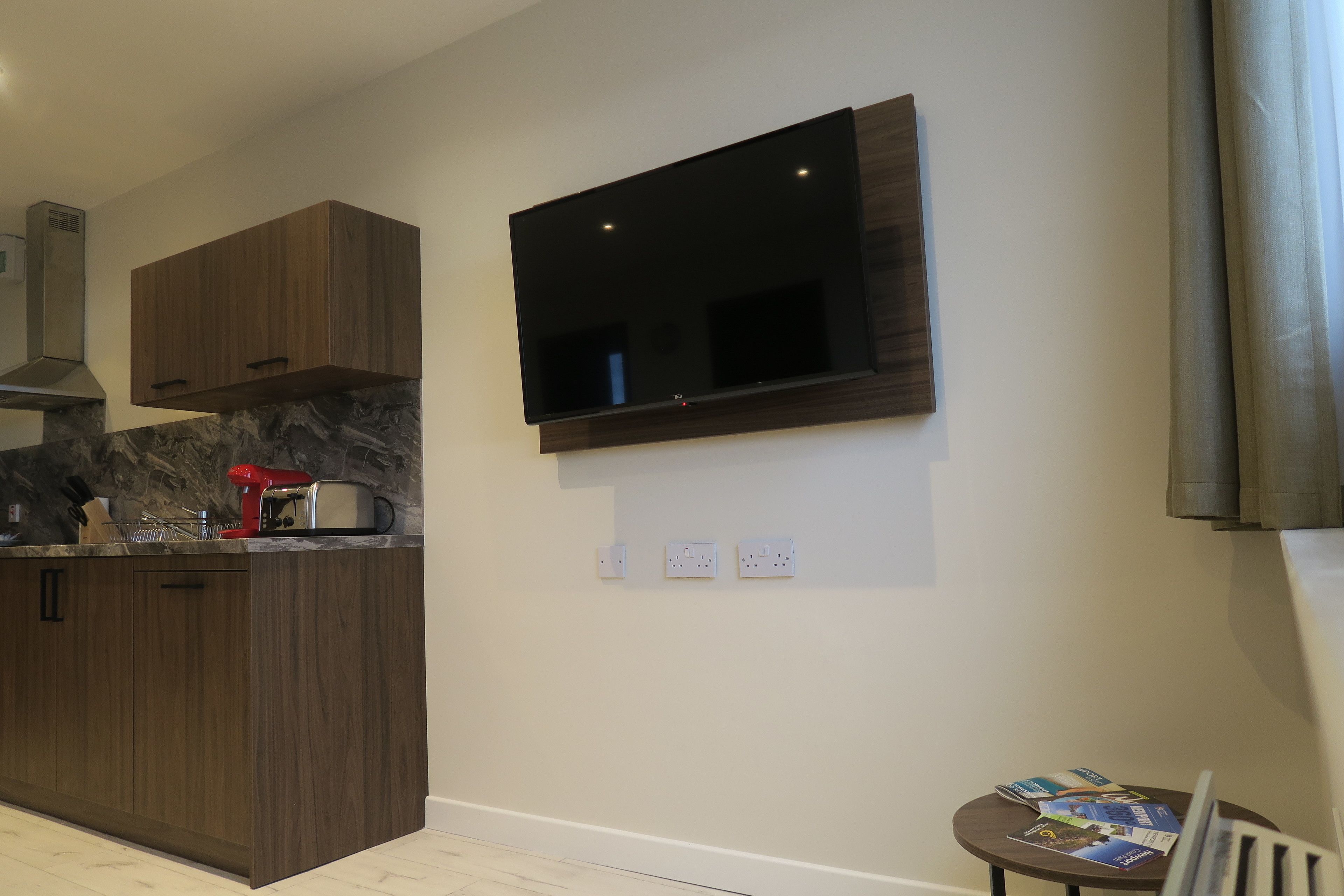 A modern kitchen with wooden cabinets, a built-in stove, and a flat-screen TV mounted on the wall.