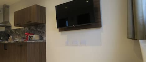 A modern kitchen with wooden cabinets, a built-in stove, and a flat-screen TV mounted on the wall.