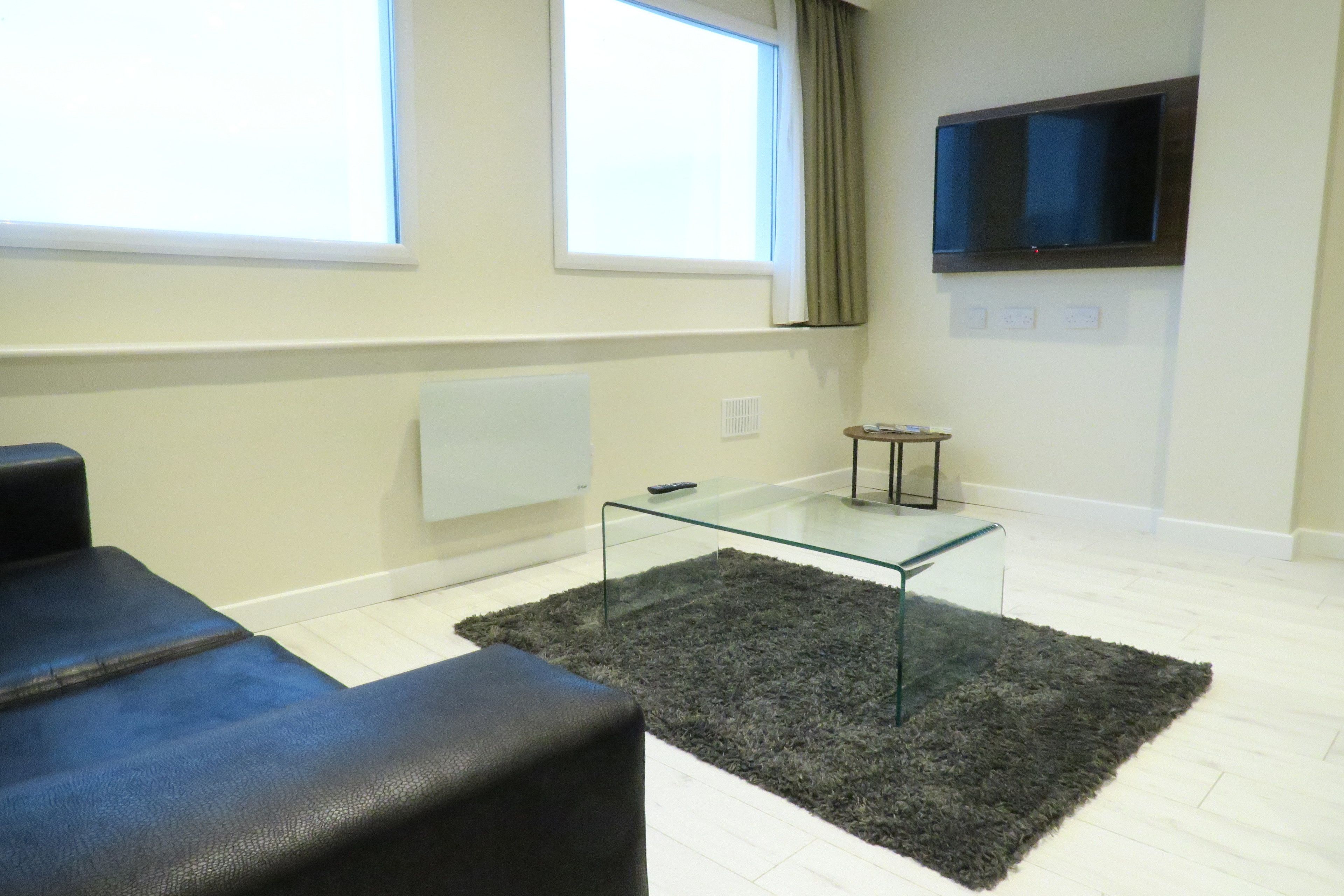 Una sala de estar moderna con una mesa de centro de vidrio, un sofá negro y un amplio ventanal con cortinas.