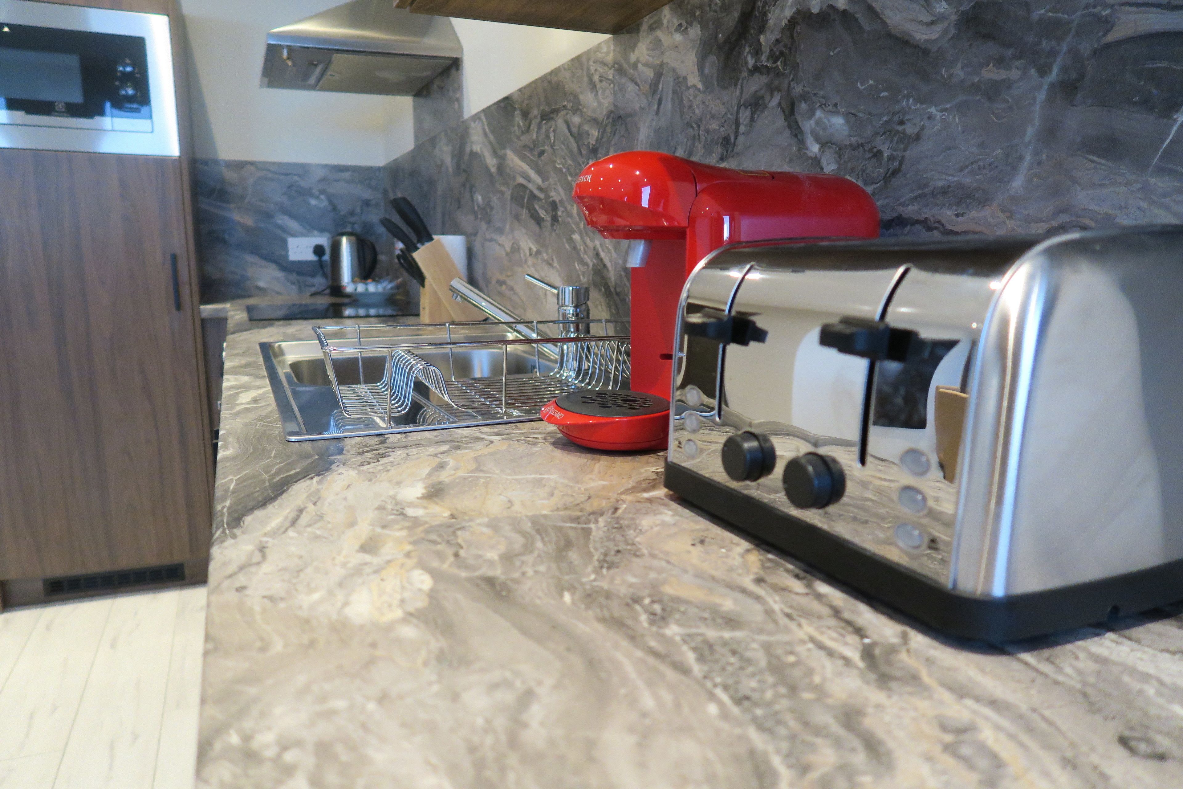 A kitchen with a marble countertop, a red food processor, a toaster, and a stainless steel kettle.