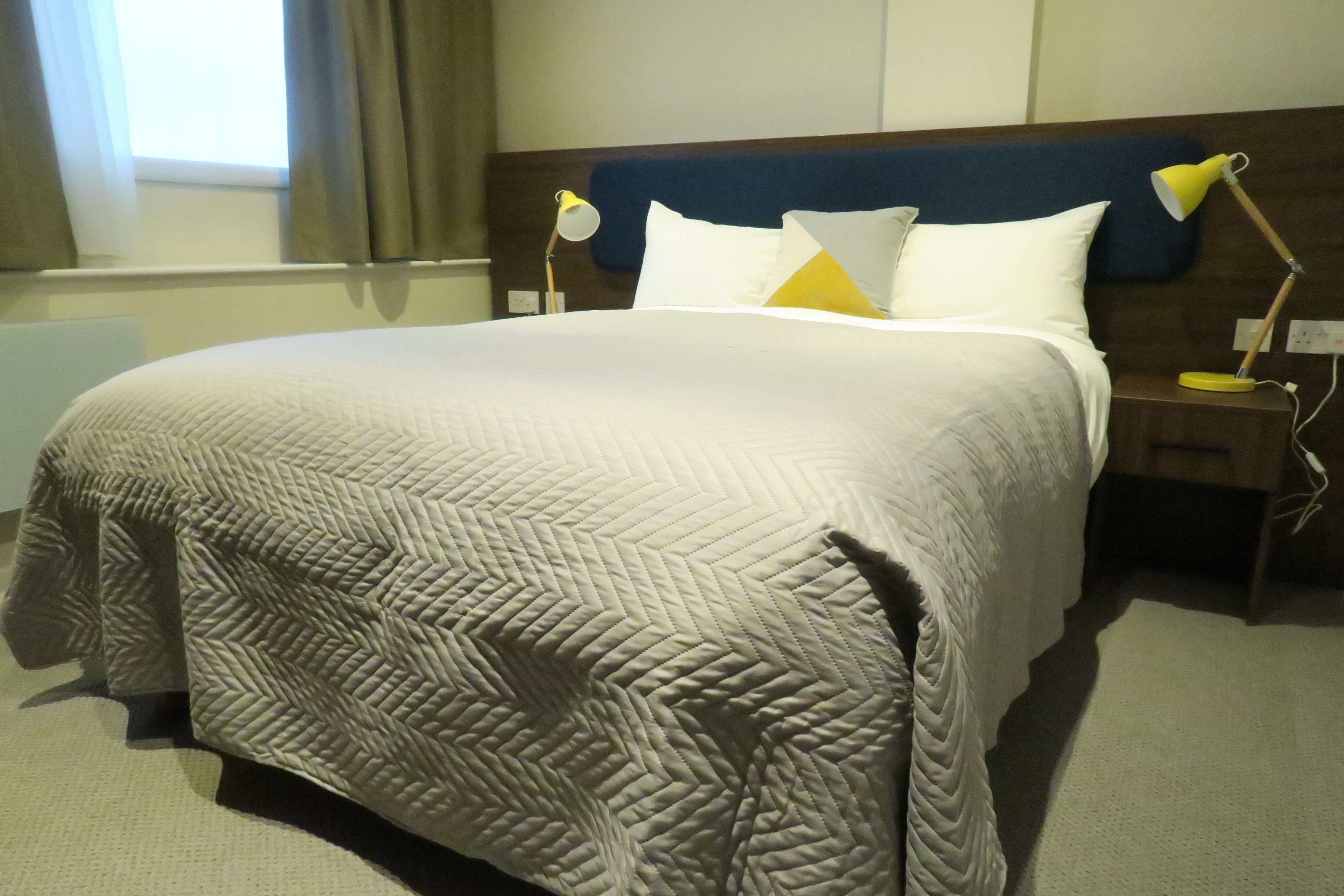 A neatly made bed with a patterned quilt, two bedside lamps, and a window with curtains.