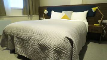 Una cama bien tendida con un edredón estampado, dos lámparas de noche y una ventana con cortinas.