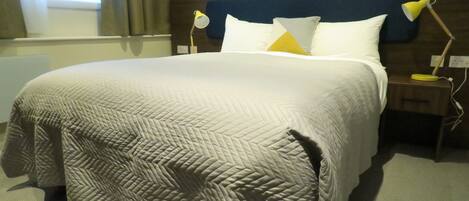 A neatly made bed with a patterned quilt, two bedside lamps, and a window with curtains.