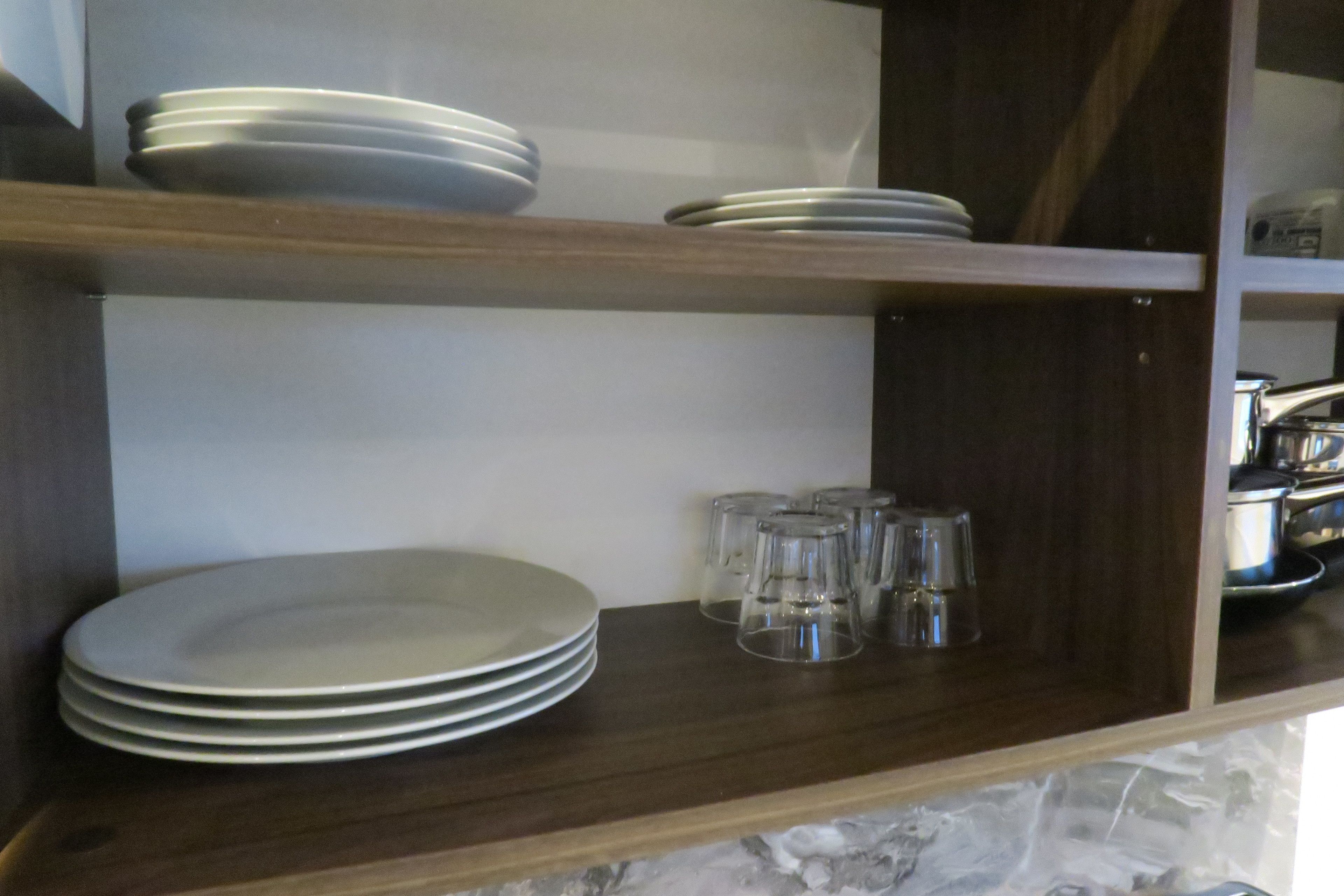 A kitchen shelf with stacked plates and clear drinking glasses.