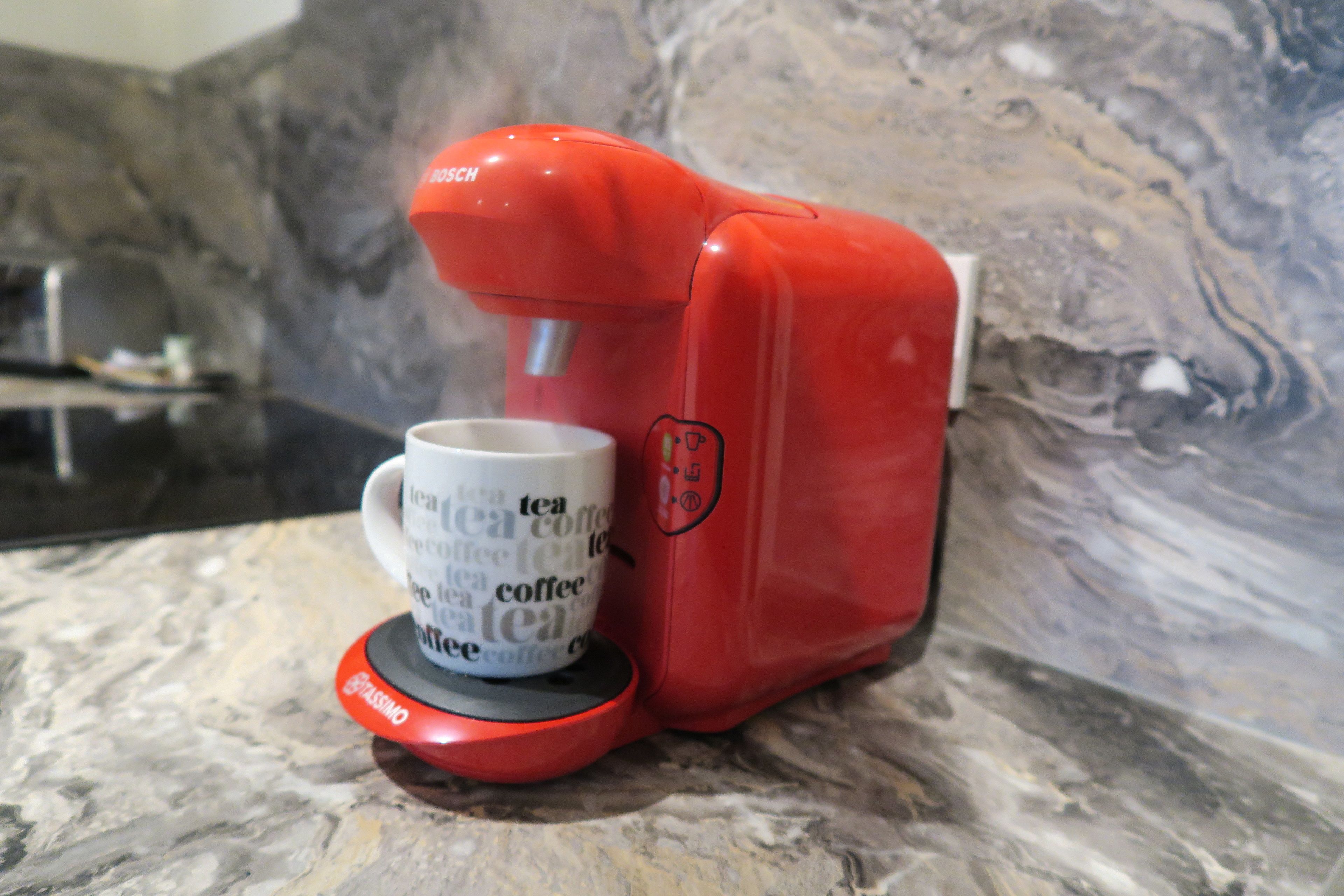 Uma cafeteira vermelha com uma chávena na base.